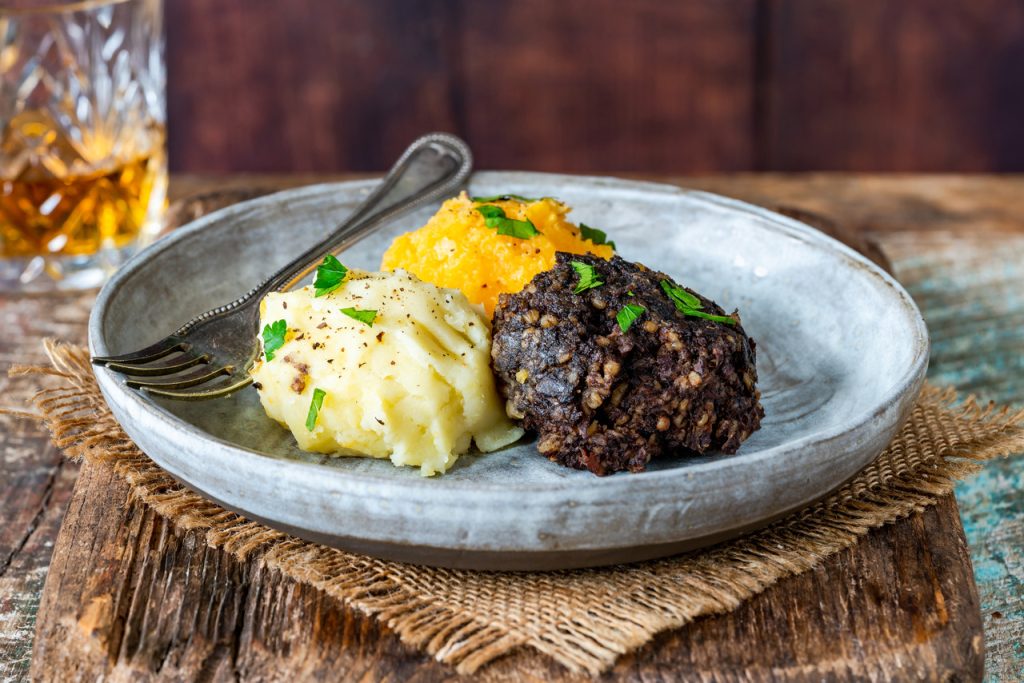 Haggis, neeps and tatties on a plate with whisky in the background
