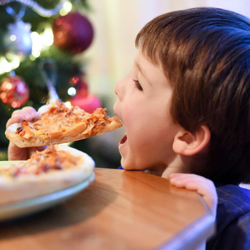 Boy eats pizza in front of Christmas tree